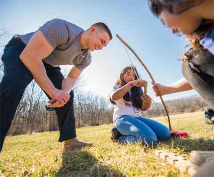 Wiltsie watches as fifth-graders Cindy Garcia (center) and Bella Davila try to make fire with rope and stick. 