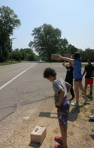 Students measure air quality from a curb next to a major road.